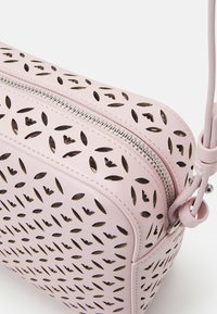 Różowa skórzana torba z wyciętymi wzorami liści, srebrnym zamkiem błyskawicznym i zaokrąglonym kształtem. Posiada odpinany pasek dla większej wszechstronności.