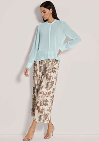 Helles Blau, durchsichtige Bluse mit Knopfleiste, kombiniert mit einem blumigen, beigen Maxirock in Erdtönen. Transparentes Material und lange Ärmel.