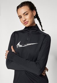 Black quarter-zip pullover made from soft, stretchy fabric, featuring a white logo on the front and thumbhole cuffs for added coverage.