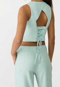 Un top corto verde menta con escote redondo, espalda abierta y detalle de cordones. Combinado con pantalones de talle alto a juego.