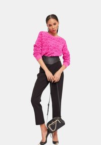 Maglione rosa con motivo e scritte nere, abbinato a pantaloni neri a vita alta e una piccola borsa a tracolla nera. Tacchi alti completano il look.