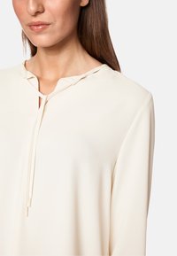 Langärmlige Bluse in Cremefarbe aus glattem Material, mit einem Schlüssel-ausschnitt und einem Halsband sowie subtilen Drapierungen.