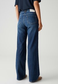 Weite dunkelblaue Jeans mit glattem Denim-Oberfläche, ausgestattet mit zwei Gesäßtaschen und einem Etikett am Bund.