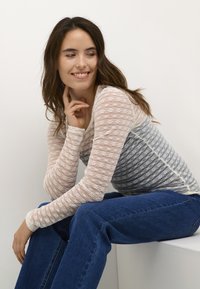 Langarm, gestreepte top in wit en grijs, met een textuur van kant. Ggedragen met blauwe jeans, wat een casual uitstraling benadrukt.