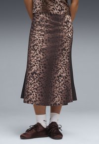 Person iført en brun nederdel med leopardprint, matchende top, hvide crewstrømper og mørkebrune snørestøvler, stående mod en grå baggrund.