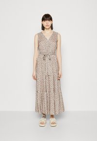 Maxikleid aus weichem beigen Stoff mit weißem Blattmuster, V-Ausschnitt, tailliertem Bund und gestuftem Rock. Kombiniert mit Plateausandalen.