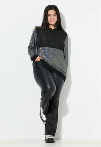 Zwarte sequined hoodie met een glanzend zilveren accentpaneel, gecombineerd met zwarte leren broek en zilveren laarzen.