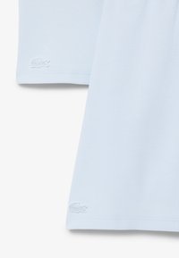 Camisa polo de rayas azul claro con mangas cortas, que presenta un pequeño logotipo bordado en blanco cerca del dobladillo. Textura suave, diseño de cuello clásico.