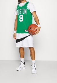 Camiseta de baloncesto verde con "BOSTON" y el número "8", combinada con pantalones cortos blancos que presentan un logo negro de Nike, y zapatillas blancas de Nike.