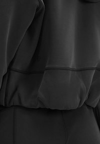 Black athletic hoodie with smooth fabric, featuring a zippered pocket and elastic hem. Visible stitching accents enhance the design.