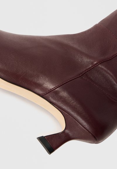 Bordeaux leren enkellaars met een gebogen silhouet, puntige neus en een 7,5 cm hoge stilettohak. Gladde textuur met subtiele stikdetails.