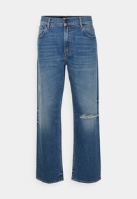 Μπλε τζιν παντελόνι καμπάνα με ψηλή μέση, μπροστινό κουμπί, τσέπες και μια φθορά στο δεξί μηρό.