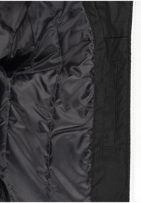 Intérieur de veste isolante noire avec tissu lisse, texture matelassée, poche latérale et fermeture éclair blanche contrastante.