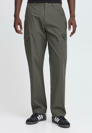 Pantalons cargo en vert olive, en tissu de coton, présentant des poches latérales, des jambes droites et une fermeture éclair, associés à des baskets noires.