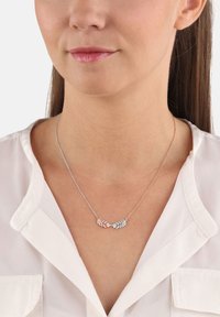 Collana a pendente in argento e oro rosa con una delicata catena, caratterizzata da intricati disegni di foglie e dettagli. Indossata su una blusa bianca.