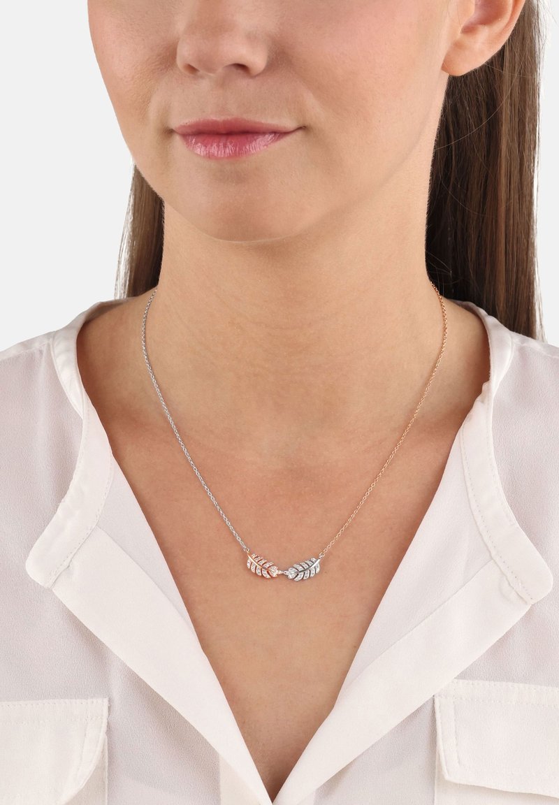 Collana a pendente in argento e oro rosa con una delicata catena, caratterizzata da intricati disegni di foglie e dettagli. Indossata su una blusa bianca.