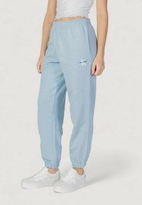 Světle modré tepláky s elastickými manžetami a pasem na šňůrku, s bílým logem Calvin Klein na levém stehně.