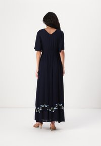 Navy blue maxi dress with a V-back and short sleeves; features floral embroidery at the hem and a gathered waistband for shape.
