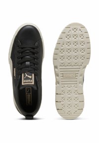 Sneaker nera con upper in pelle textured, suola in gomma beige e lacci piatti. Presenta dettagli con logo e una suola con motivo geometrico.