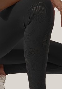 Svarta leggings med ett texturerat blommönster längs den yttre låret, tillverkade av stretchigt tyg med en jämn yta.