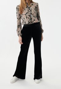 Pantalons évasés en velours noir associés à un haut à manches longues en imprimé paisley multicolore, comportant un détail de bouton au niveau du col et des manches à poignets.