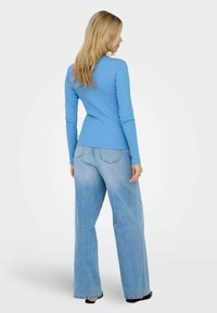 Lyseblå langermet topp kombinert med løstsittende lyse denimjeans. Toppen har et enkelt design, og jeansene har en falmet finish.