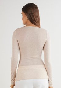 Långärmad topp i ljusbeige, tillverkad av mjukt, lättviktigt material. Har rundad halslinning och figursydd design, slät textur.