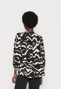 Blusa com padrão preto e rosa, de corte solto, mangas longas e design com pregas nas costas. Tecido suave, gola redonda e punhos elásticos.