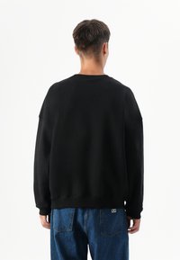 Zwarte sweatshirt met een ontspannen pasvorm, geribbelde manchetten en een ronde hals, gecombineerd met blauwe denim jeans met achterzakken en stiksel details.