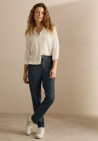 Lättviktig vit skjorta med vertikala ränder, i kombination med mörkblå joggingbyxor med justerbar dragsko och vita sneakers.