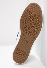 Pohja tummansinisten ja valkoisten Converse All Star -tennareiden, joissa on näkyvä röpelöinen ruskea kumipohja.