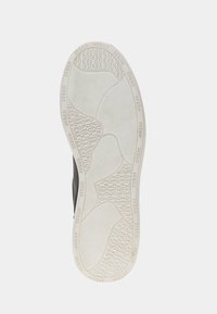 Schuhsohle mit einer strukturierten, weißen GummOberfläche, die ein ineinandergreifendes Wellenmuster aufweist und mit "GUESS"-Markenakzenten versehen ist.