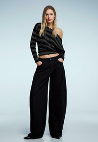 Fekete, széles szárú nadrág, fekete-ezüst csíkos, váll nélküli felsővel párosítva, laza kialakítással és bordázott textúrával.