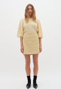 Svetlo rumena kratka majica s kratkimi rokavi v kombinaciji s krilom do kolen, ki ima rumeno in belo houndstooth vzorčevanje. Črne gležnjarje in špičaste čevlje.