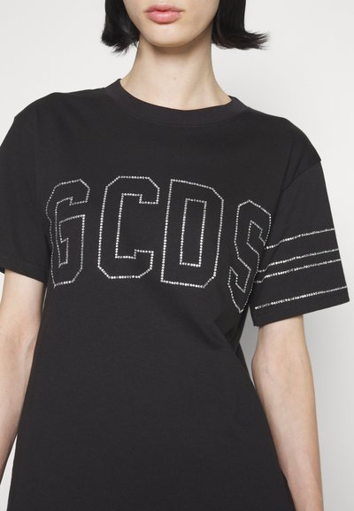 Μαύρη βαμβακερή μπλούζα T-shirt με μεγάλα γράμματα "GC" διακοσμημένα με κρύσταλλα στο μπροστινό μέρος και τρεις ασημένιες ρίγες στα μανίκια. Κοντά μανίκια, στρογγυλή λαιμόκοψη.