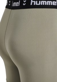 Dopasowane, jasnooliwkowe legginsy z czarnym pasem w talii, ozdobione białym logo "hummel". Gładka tekstura w jednolitym kolorze.