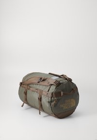 Duffle bag i olivengrønn nylon med brune detaljer. Har justerbare stropper, en glidelåslomme og en stor logo på siden.