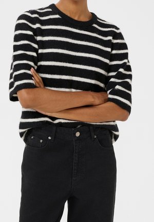 Czarnobiały sweter w paski z krótkim rękawem wykonany z miękkiego materiału, zestawiony z czarnymi dżinsami z wysokim stanem, posiadającymi dwie przednie kieszenie.