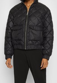 Czarna pikowana kurtka puchowa z wysokim kołnierzem, zapięciem na zamek i dwiema przednimi kieszeniami. Posiada prążkowane mankiety i skrócony krój.