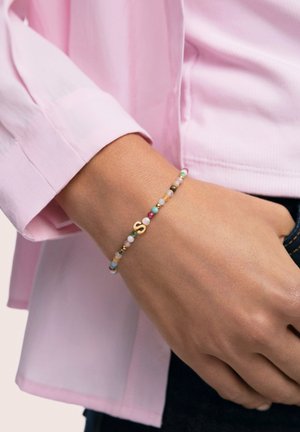 Kleurrijke kralenarmband met roze, groen en gouden accenten, voorzien van een kleine gouden letter 'S' bedel, gedragen om een pols.