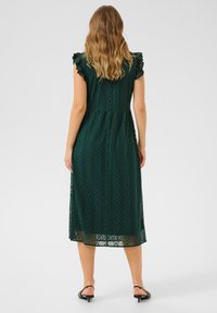 Green lace dress with short, ruffled sleeves. Features a fitted bodice, a flared skirt, and a geometric pattern with a scalloped hem.