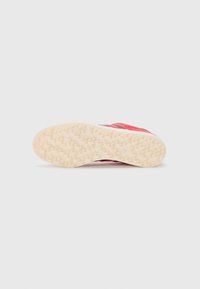 Red athletic shoe with a textured rubber sole featuring a honeycomb pattern. Upper includes a smooth fabric and logo accents.