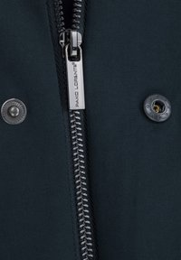 Element w ciemnoniebieskiej kurtce z metalowym zamkiem błyskawicznym z metką logo oraz okrągłym zatrzaskiem, przekazujący szczegóły tekstury materiału.