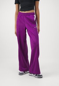 Purple athletic pants with an elastic waistband, side pockets, and white accent details. Made of smooth, lightweight fabric.