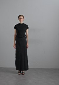 Black sleeveless top with a high neckline, paired with a long black skirt and black open-toe sandals. Smooth texture, minimalist design.