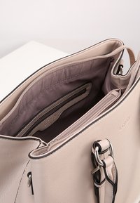 Jasno beżowa skórzana torebka z zamkiem błyskawicznym u góry, wewnętrznymi kieszeniami oraz ciemnym przeszyciem. Gładka tekstura i wyrafinowany kształt.