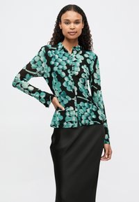 Camisa preta de botões com um padrão floral abstrato em verde e turquesa, feita de um tecido leve com uma textura suave e mangas longas.