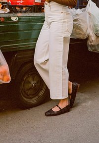 Jeans blancos de cintura alta con un ajuste relajado y detalles de bolsillos, combinados con unos zapatos Mary Jane negros brillantes con correas al tobillo.