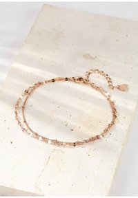 Bransoletka w kolorze różowego złota, z delikatnymi łańcuszkami, płaskimi i okrągłymi koralikami, teksturowanymi akcentami oraz z zapięciem w postaci kraba z przedłużanym łańcuszkiem.