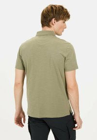 Oliven grøn polo shirt med korte ærmer, afslappet krave og sideslids, lavet af letvægtsstof. Modellen vender væk fra kameraet og viser detaljerne på ryggen.